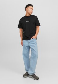 Black cotton t-shirt with short sleeves and a white logo, paired with light blue loose-fitting jeans and grey athletic shoes.