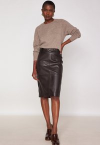 Gonna a matita in pelle marrone con vita cinturata, caratterizzata da una texture liscia, dettagli delle cuciture e un taglio al ginocchio, abbinata a un maglione beige.