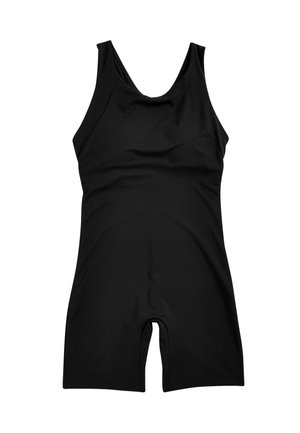 Kobieta z warkoczami, ubrana w czarny dopasowany, bezrękawnikowy kombinezon, stojąca na zewnątrz na tle białego architektonicznego tła i niebieskiego nieba.