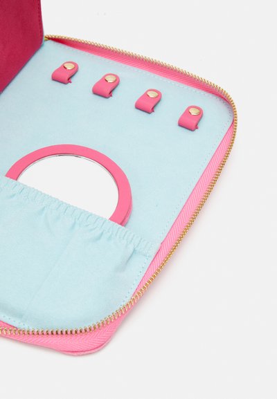 Pink zippered case with a blue interior, featuring three pink straps and a circular mirror. Soft texture and gold hardware accents.