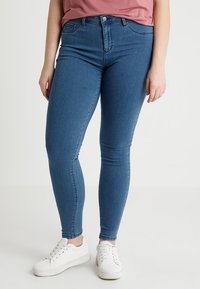 Skinny blue jeans made of denim, featuring a classic five-pocket design, mid-rise waist, and paired with white sneakers.
