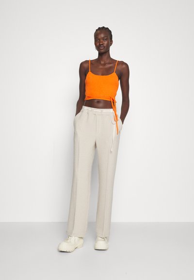 Πορτοκαλί πλεκτό cropped τοπ με λεπτές τιράντες και λεπτομέρεια δεσίματος, συνδυασμένο με ανοιχτό γκρι παντελόνι με φαρδιά γραμμή και χοντρές μπεζ αθλητικές μποτές.