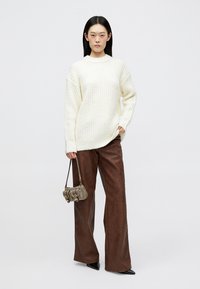 Maglione lavorato a maglia bianco spesso, pantaloni a gamba larga in pelle marrone e piccola borsa argento con dettagli in metallo. Tessuto liscio e vestibilità comoda.