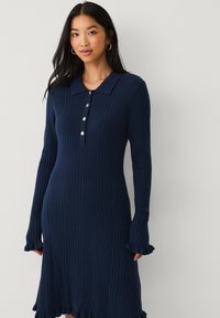 Marineblaues geripptes Strickkleid mit langen Ärmeln, einem Polokragen und Knopfleiste; verfügt über einen gerafften Saum und Ärmelabschlüsse für zusätzliche Textur.