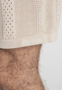 Gehaakte beige shorts met een textuur en stippenpatronen. De onderzoom toont de "GIANNI KAVANAGHI" branding in witte draad.