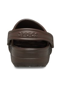 Sabots en caoutchouc marron Crocs avec une sangle arrière, dotés d'une semelle rugueuse pour une meilleure adhérence, d'une forme arrondie et du logo "crocs" sur la sangle.