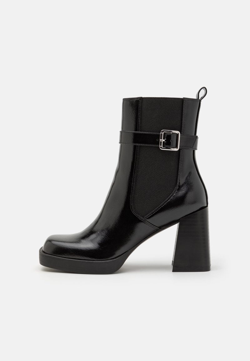 Bottine en cuir noir brillant avec talon carré, panneau élastique latéral, sangle décorative avec boucle et languette à l'arrière.