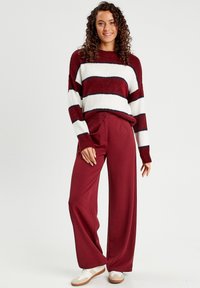 Pull rayé marron avec des lignes blanches et bleu marine ; associé à un pantalon taille haute marron ; baskets blanches ; texture douce, coupe décontractée.