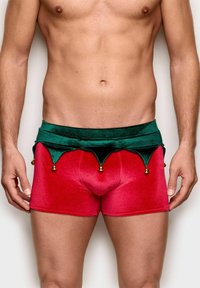 Røde velvet-shorts med en grøn velvet-linning. Linningen har spidse kanter og gyldne klokker. Glat tekstur, tætsiddende design.