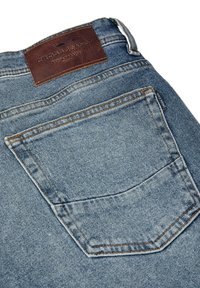 Vaqueros de mezclilla azul con un bolsillo trasero prominente, costuras naranjas contrastantes y una etiqueta de cuero marrón grabada con "CROSS JEANS."