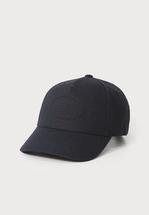 Marineblå baseballcap laget av stoff, med et teksturert sirkulært merke med ordet "BOSS" i svart, buet skjerm og broderte detaljer.