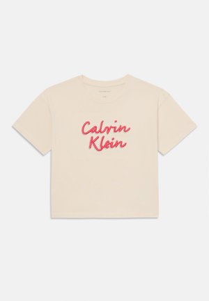Trumpas rankovės, kreminės spalvos pasėlių marškinėliai su siuvinėtu raudonu "Calvin Klein" logotipu per krūtinę; minkšta medvilninė medžiaga, apvalus iškirpimas.