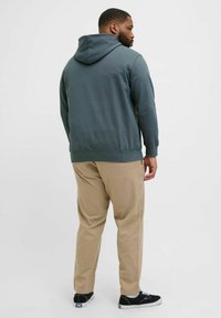 Mørkegrøn sweatshirt med hætte og snoretræk, kombineret med lysebeige bukser. Modellen har sorte sko med hvide detaljer på.