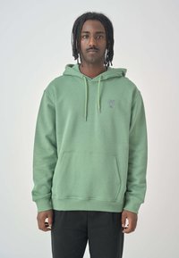 Mint green hoodie made of soft fabric, featuring a kangaroo pocket, adjustable drawstrings, and a small purple logo on the chest.