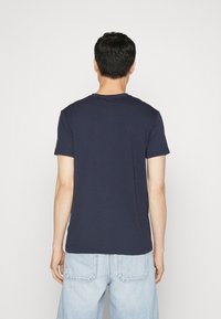 Camiseta de algodón azul marino de manga corta con cuello redondo, mostrando la vista posterior. Corte ajustado, textura lisa y sin patrones ni acentos visibles.