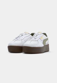 Zapatillas blancas con suela de plataforma, detalles en verde oliva y textura suave. Presentan cordones planos y un logo en el lateral.
