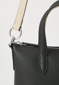 Black textured leather handbag with a smooth zipper, cream-colored fabric strap, and silver hardware detailing. Features a structured shape.