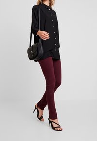 Black long-sleeve shirt with buttons, paired with burgundy fitted pants and black strappy heels. Includes a small black crossbody bag.