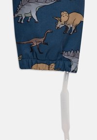 Tecido azul com várias ilustrações de dinossauros em tons de bege e cinza, com um punho elástico e uma etiqueta branca anexada na parte inferior.