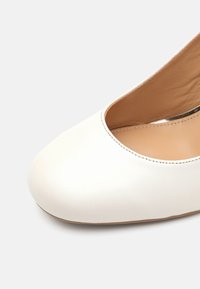 Chaussure plate en cuir blanc pour femme, à bout arrondi et doublure intérieure beige sur fond clair.