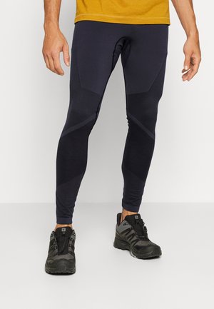 Die marineblauen Performance-Leggings zeichnen sich durch ein eng anliegendes Design mit strukturierten Akzentpaneelen und einer glatten Oberfläche aus. Sie werden mit schwarzen Trail-Laufschuhen kombiniert.