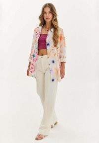 Viacfarebná tričko s farbeným vzorom a gombíkmi, s vyhrnutými rukávmi, nosené cez ružový crop top a skombinované s krémovými širokými nohavicami a sandálmi.