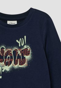 Marineblauw langemouwen shirt met een grafische print en de tekst "BESCHERM DE TOEKOMST" in vet rood en wit, met cirkelvormige spuitverfaccenten.