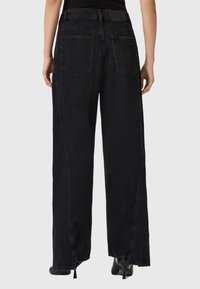 Black wide-leg jeans made of denim, featuring a classic five-pocket design and visible stitching, with a waistband label at the back.