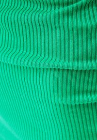 Tissu vert côtelé avec des lignes parallèles texturées, présentant un matériau doux, extensible et une finition lisse.