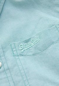 Svetlo modra srajca s kratkimi rokavi iz teksturirane tkanine, z sprednjo žepono in izvezenim logotipom "SuperDry".