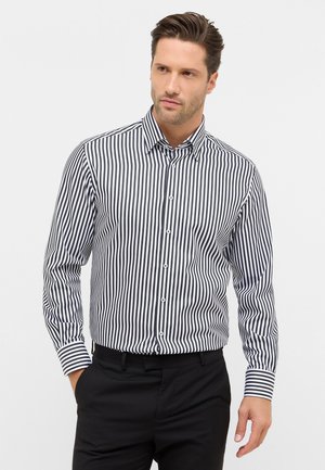 Camicia a maniche lunghe con righe verticali bianche e nere, dotata di colletto classico, abbinata a pantaloni neri.