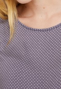 Marinblus med rund halsringning, med ett litet blommönster i ljuslila. Slät tyg med en lätt stretch och subtil lyster.