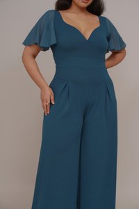 Türkisfarbener Jumpsuit mit tailliertem Oberteil, V-Ausschnitt und transparenten Flügelärmeln; weit geschnittenes Design mit Vorderfalten und Taschen.