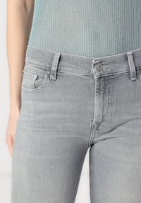 Jeans in denim grigio con un design aderente, due tasche frontali, chiusura con bottone e una trama sottile. Hanno un girovita a vita media.