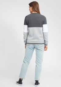 Felpa color bloc in grigio e bianco con una texture morbida, collo rotondo e polsini a costine, abbinata a jeans blu chiaro strappati e sneaker alte nere.