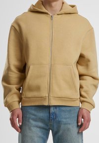Kapuzensweatshirt mit Reißverschluss in hellbeige, aus weichem Stoff. Mit zwei Fronttaschen sowie gerippten Bündchen und Saum. Lässiges Design.