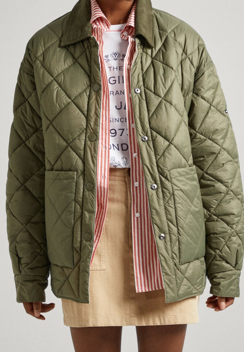 Chaqueta acolchada verde oliva con patrón de diamantes, cierre de botones y bolsillos de parche, combinada con una camisa de rayas y una falda beige.