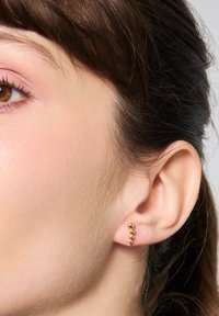 Złote kolczyki o kaskadowym wzorze z kulistymi akcentami, noszone w płatku ucha, prezentujące błyszczące wykończenie i gładką fakturę.