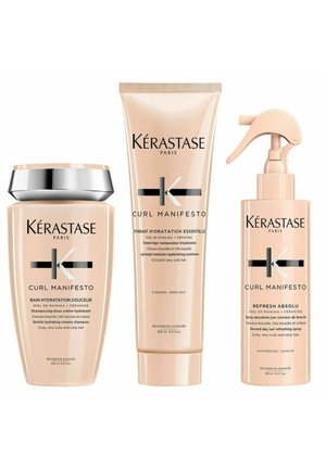 Three Kérastase Curl Manifesto products: a pale pink shampoo with a silver cap, a matching conditioner, and a leave-in spray with a trigger nozzle.