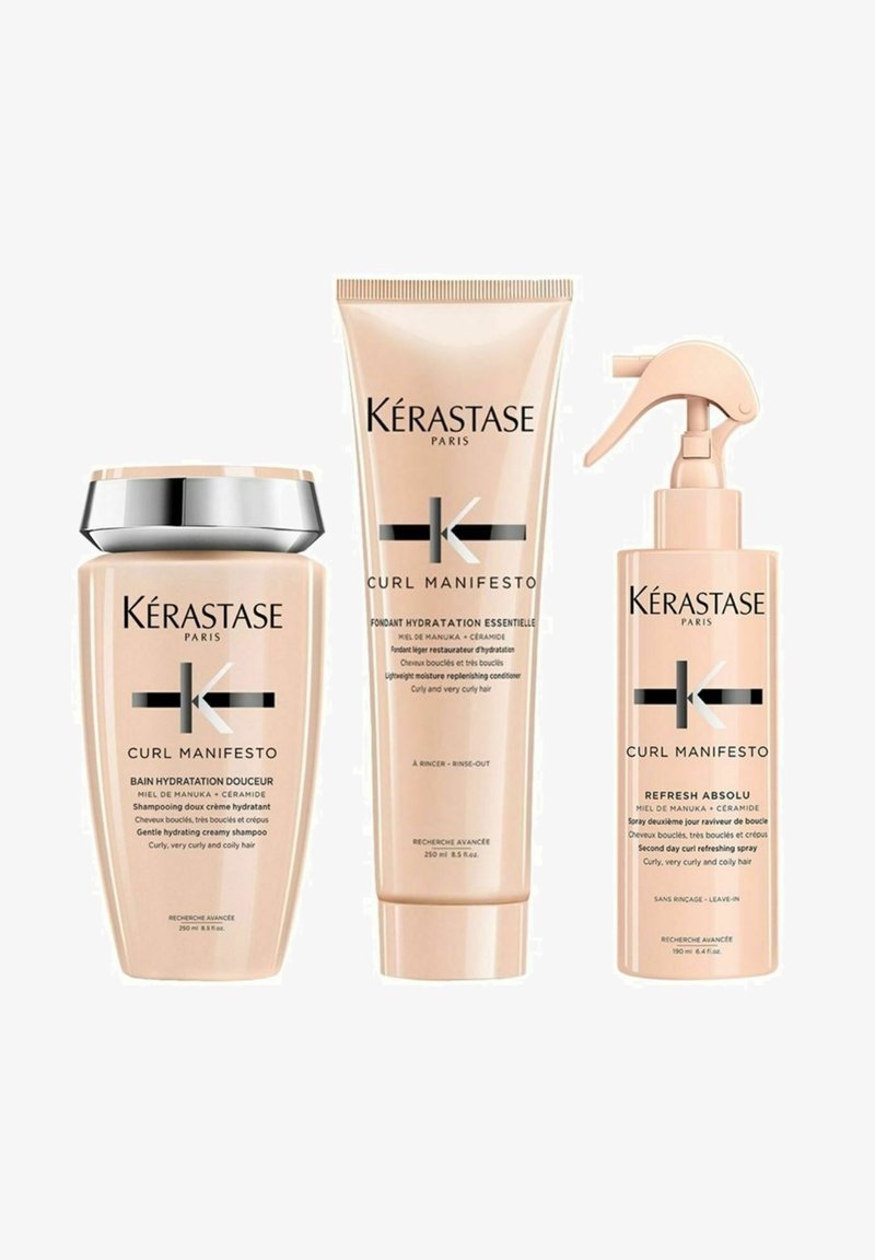 Three Kérastase Curl Manifesto products: a pale pink shampoo with a silver cap, a matching conditioner, and a leave-in spray with a trigger nozzle.