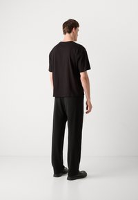 Schwarzes T-Shirt mit kurzen Ärmeln kombiniert mit schwarzen Hosen. Minimalistisches Design, lässige Passform, aus weichem Stoff gefertigt. Glatte Textur, robustes Schuhwerk.