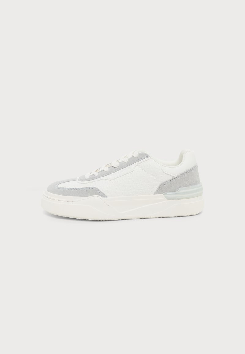 Baskets basses blanches avec accents en daim gris, fermeture à lacets et semelle épaisse, vues de profil sur un fond uni.