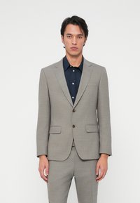 Ανοιχτό γκρι �σακάκι με κομμένο άνετο σχέδιο, μονόστρας, με κλείσιμο δύο κουμπιών και ανακλινόμενα πέτα. Συνδυάζεται με μπλε πουκάμισο με κουμπιά.