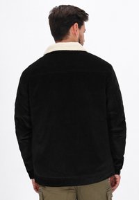 Fekete kordbársony dzseki krémszínű műbőr gyapjú gallérral, egyenes szabású és hosszú ujjú. A részletes varrás jól látható.