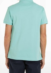 Polo shirt turchese chiaro realizzato in tessuto texture, con colletto classico e maniche corte, orlo dritto e spacchetti laterali.