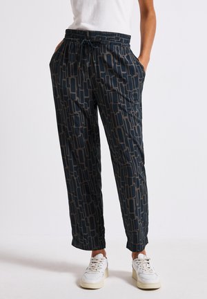 Lässiges Outfit mit gemusterten dunkelblauen Hosen mit elastischem Bund und Taschen, kombiniert mit weißen Sneakers und einem schlichten weißen Shirt.