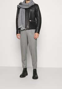 Mustaa nahkaa oleva vetoketjuhuppari, harmaa kudottu huivi, vaaleanharmaat ruutuhousut ja mustat nilkkurit. Yksinkertainen muotoilu ja rento istuvuus.