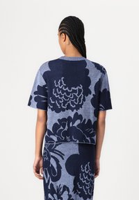 Top a maglia blu navy con maniche corte, caratterizzato da grandi motivi floreali in un blu più chiaro. Texture morbida e vestibilità rilassata.