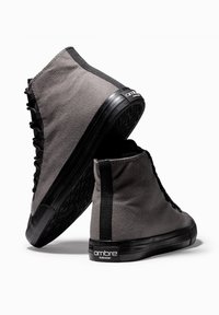 Baskets montantes en toile grise avec semelles en caoutchouc noir, dotées de lacets noirs, d'un motif texturé et d'un logo accentué sur le talon.