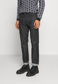 Mörkgrå denimbyxor med rak passform, uppvikta fållar och en slät yta, tillsammans med svarta snörskor i läder.